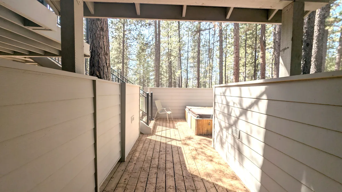 This image features a wooden deck nestled among tall trees, showcasing a private hot tub alongside inviting outdoor seating. The tranquil environment is perfect for relaxation, with serene views of nature surrounding the deck.