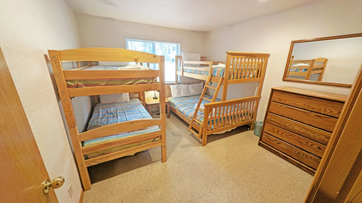 A playful bunk room styled with two sets of bunk beds, a dresser, and a window. The space is designed for fun, offering a cozy retreat for kids or families to bond and relax together.