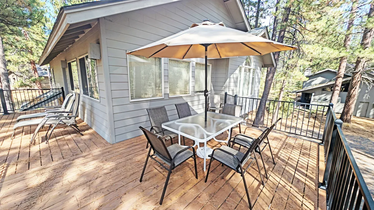 This image presents an outdoor dining table with an umbrella and deck chairs, surrounded by trees. The space is ideal for group meals, casual gatherings, and enjoying the outdoors in comfort.