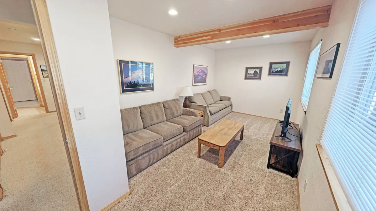 A comfortable rec room setup with a large sofa, coffee table, and a television mounted on the wall. The casual décor and soft lighting create an inviting area ideal for lounging, watching TV, or gathering for game nights and movie marathons.
