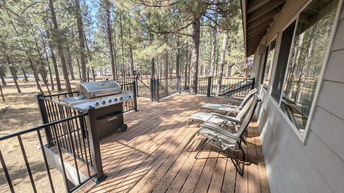 A spacious outdoor deck with inviting seating and a modern grill is surrounded by lush pine trees, creating a private retreat for barbecues and group gatherings. The deck is set up for both relaxation and socializing, with plenty of space for friends to unwind and connect with nature.