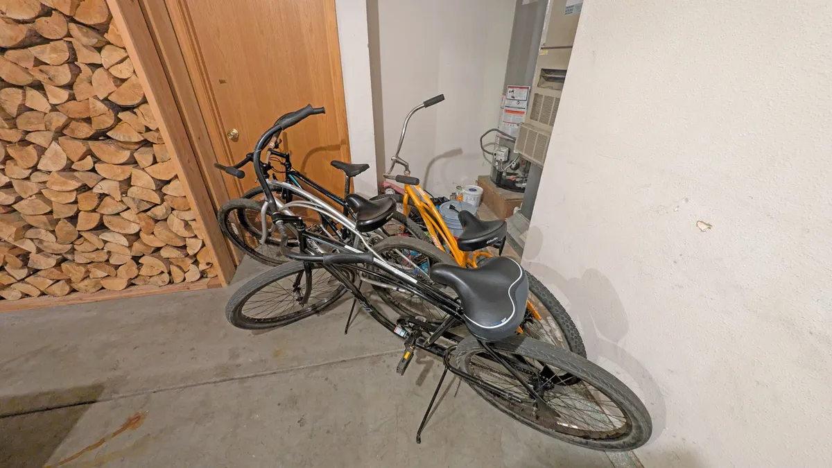 A relaxed, informal garage or mudroom area featuring several bicycles ready for use, a neatly stacked pile of firewood, and a door leading outdoors. The scene hints at easy access to outdoor adventure, with the bikes prominently displayed as a key amenity for guests.