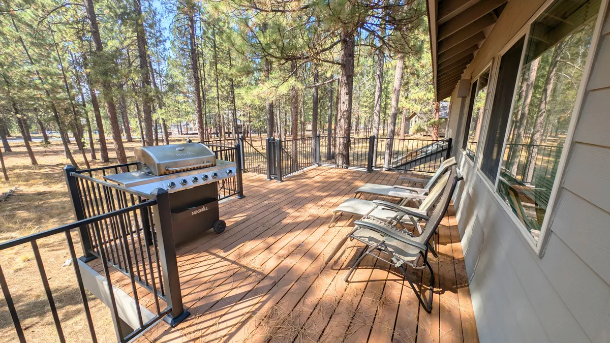 This exterior image features a wooden deck with deck chairs, a grill, and views of surrounding trees. The setting is perfect for enjoying morning coffee outdoors or hosting a barbecue, reflecting the connection between interior gathering spaces and the tranquil outdoors.