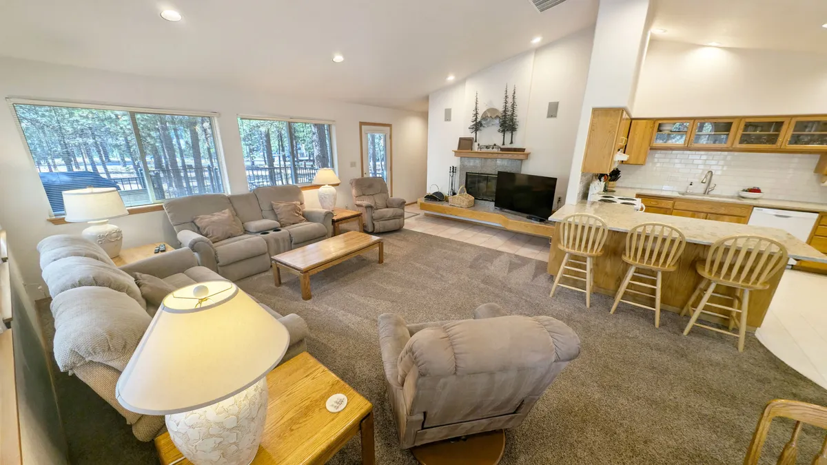 A comfortable seating area is visible near large windows, with a kitchen bar situated nearby. The space feels cozy and inviting, ideal for casual dining or relaxing with a coffee. The fireplace adds to the sense of warmth and togetherness.
