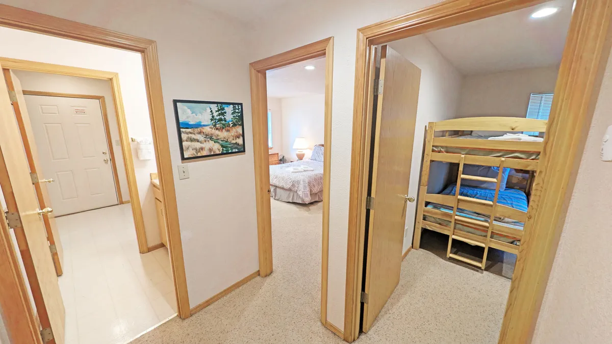 A cozy bunk room scene showing a bunk bed, a colorful painting on the wall, and doorways leading off to other bedrooms. The ambiance is playful, inviting, and designed for group or family use.